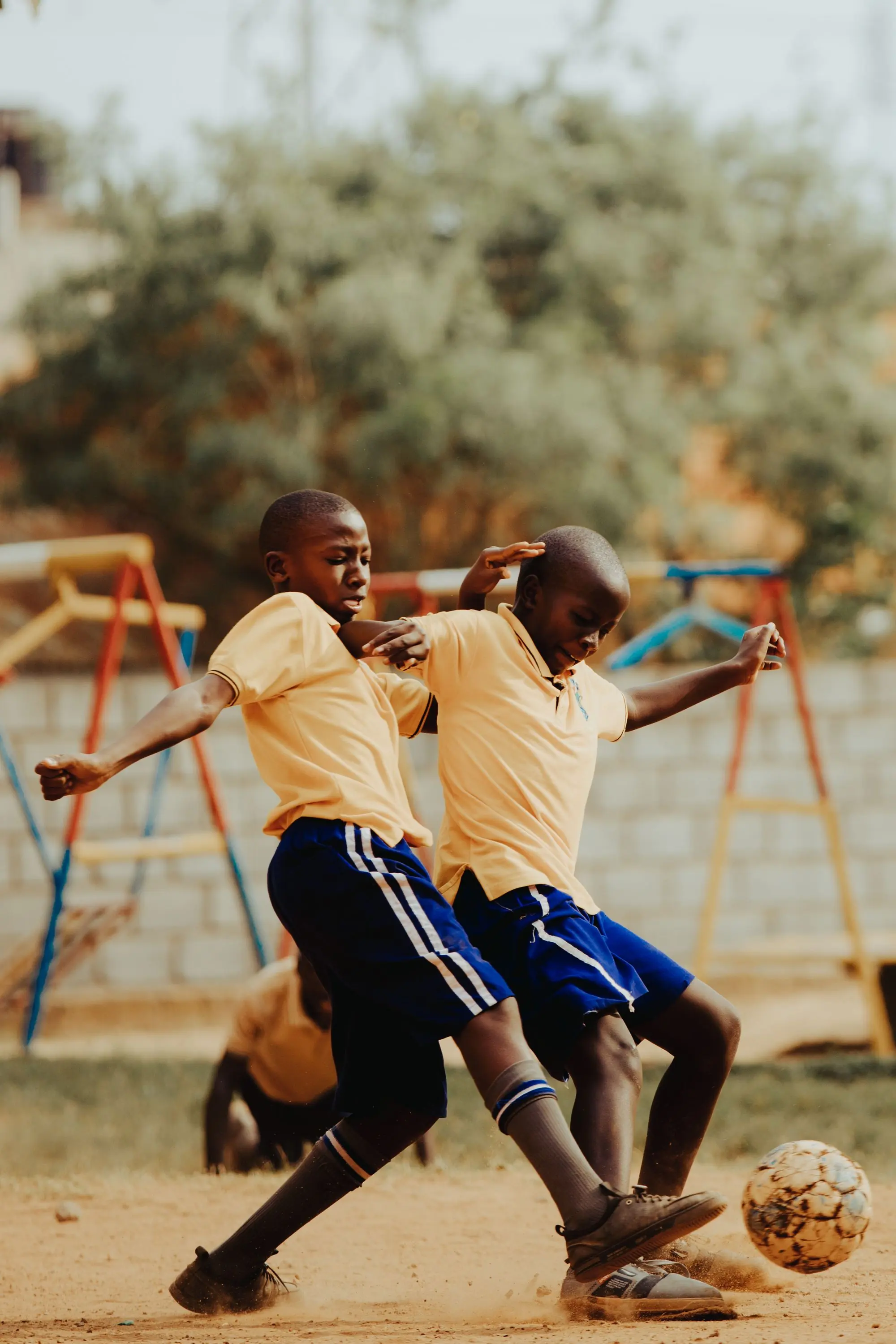 Two boys running for the ball during a football match on a bare pitch.